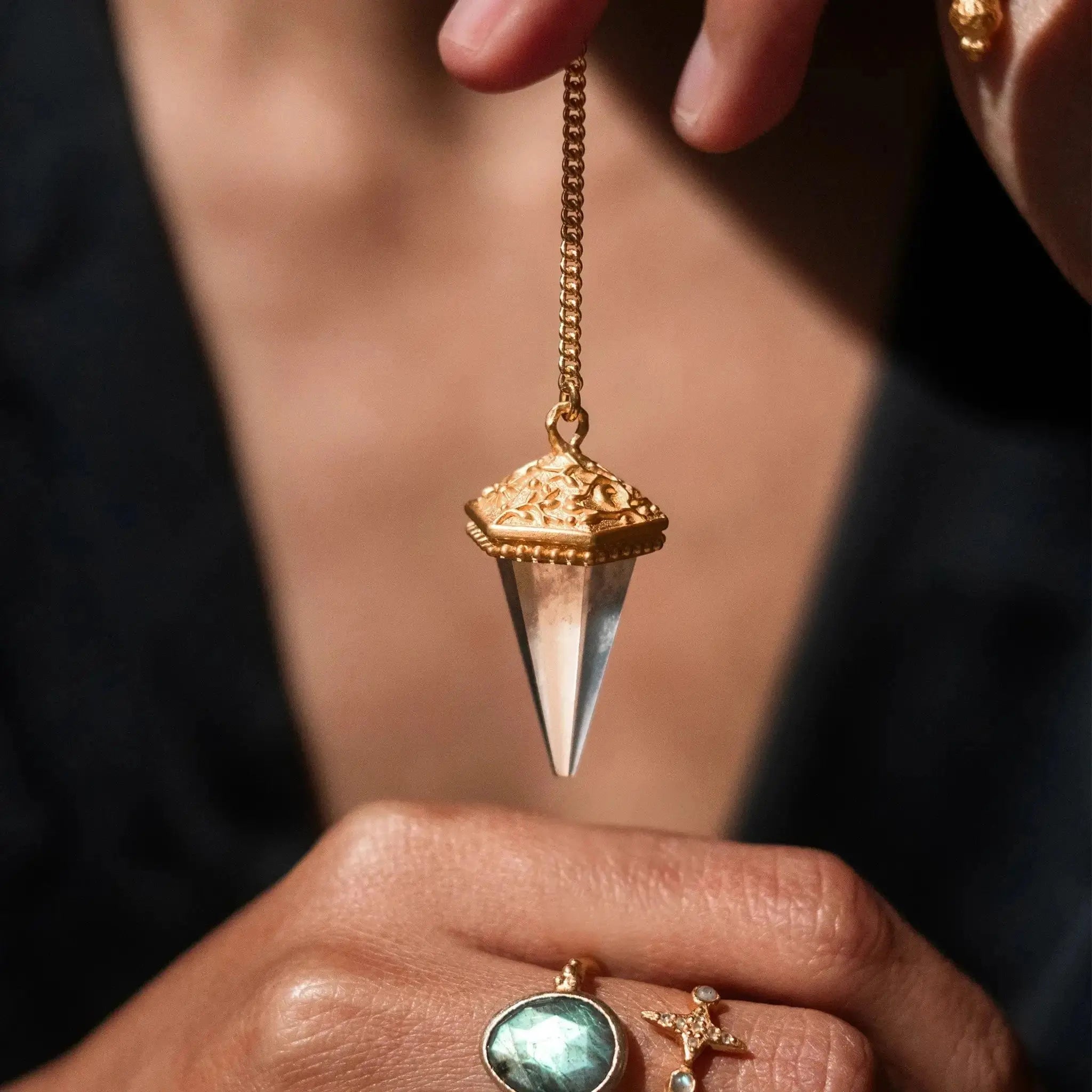 Hand holding Ananda Soul's Oracle of Light gold pendulum with crystal quartz 